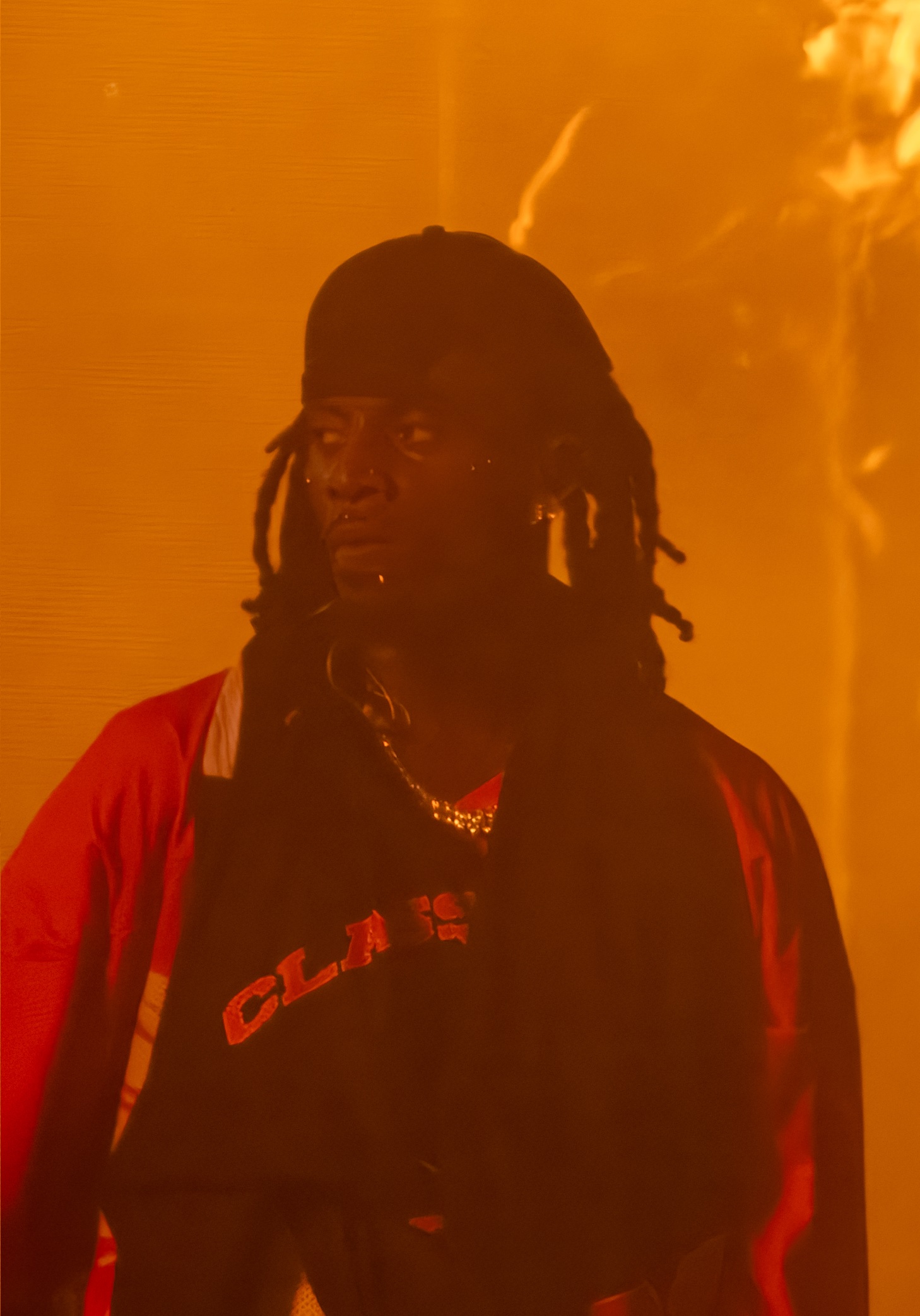 Playboi Carti in a dark outfit performing under red stage lights at Clout Festival in 2024