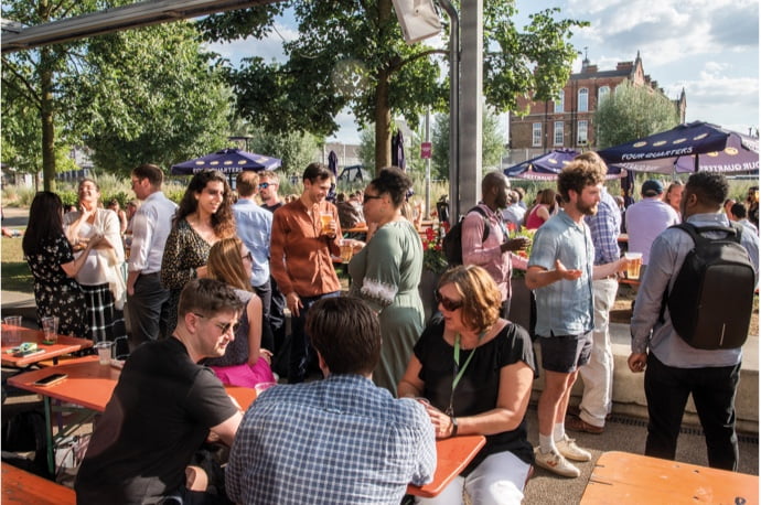 People chatting around outdoor tables in an archive photograph published by Plexal