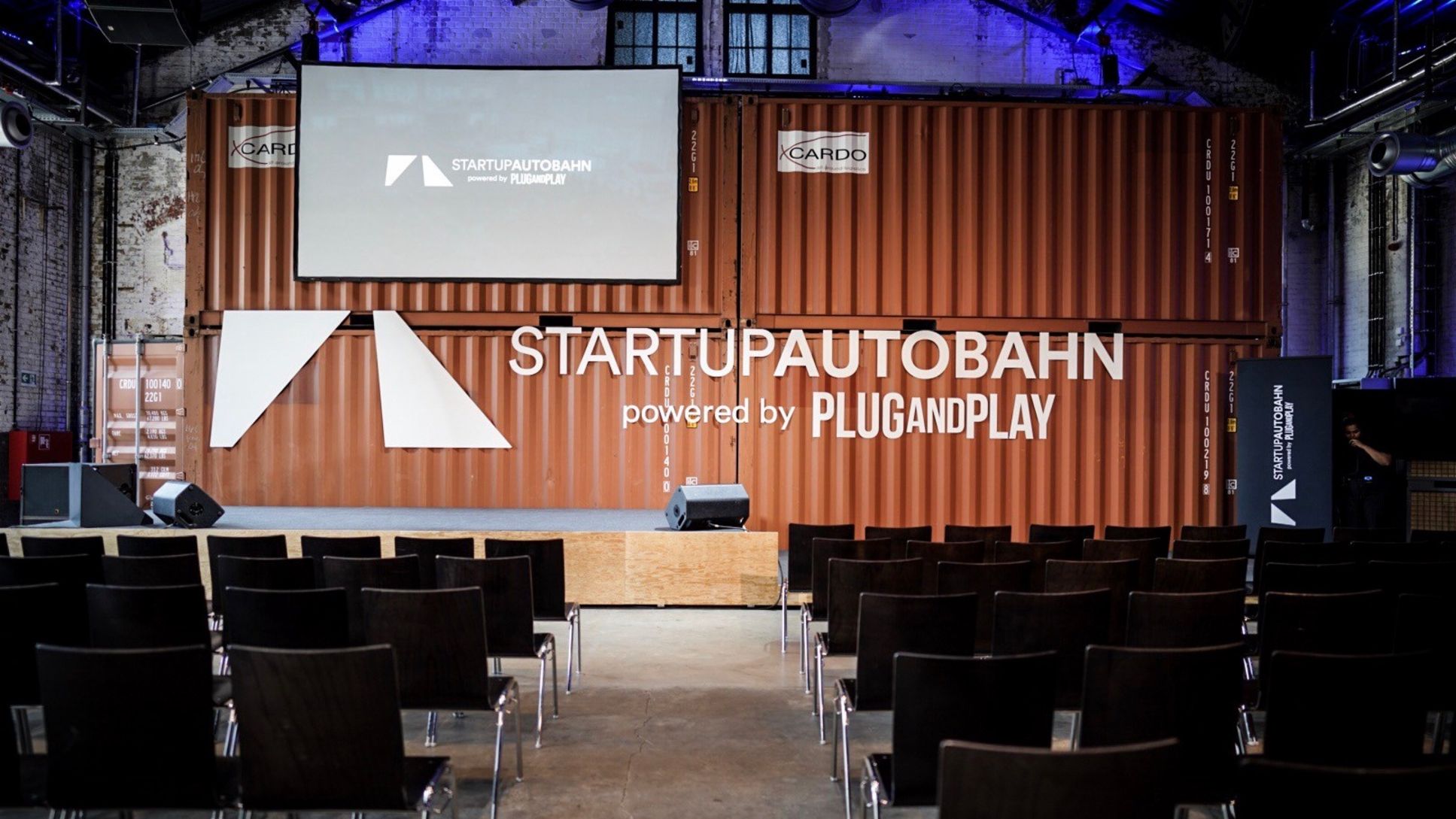 Startup Autobahn stage built around orange shipping containers, with rows of chairs in front