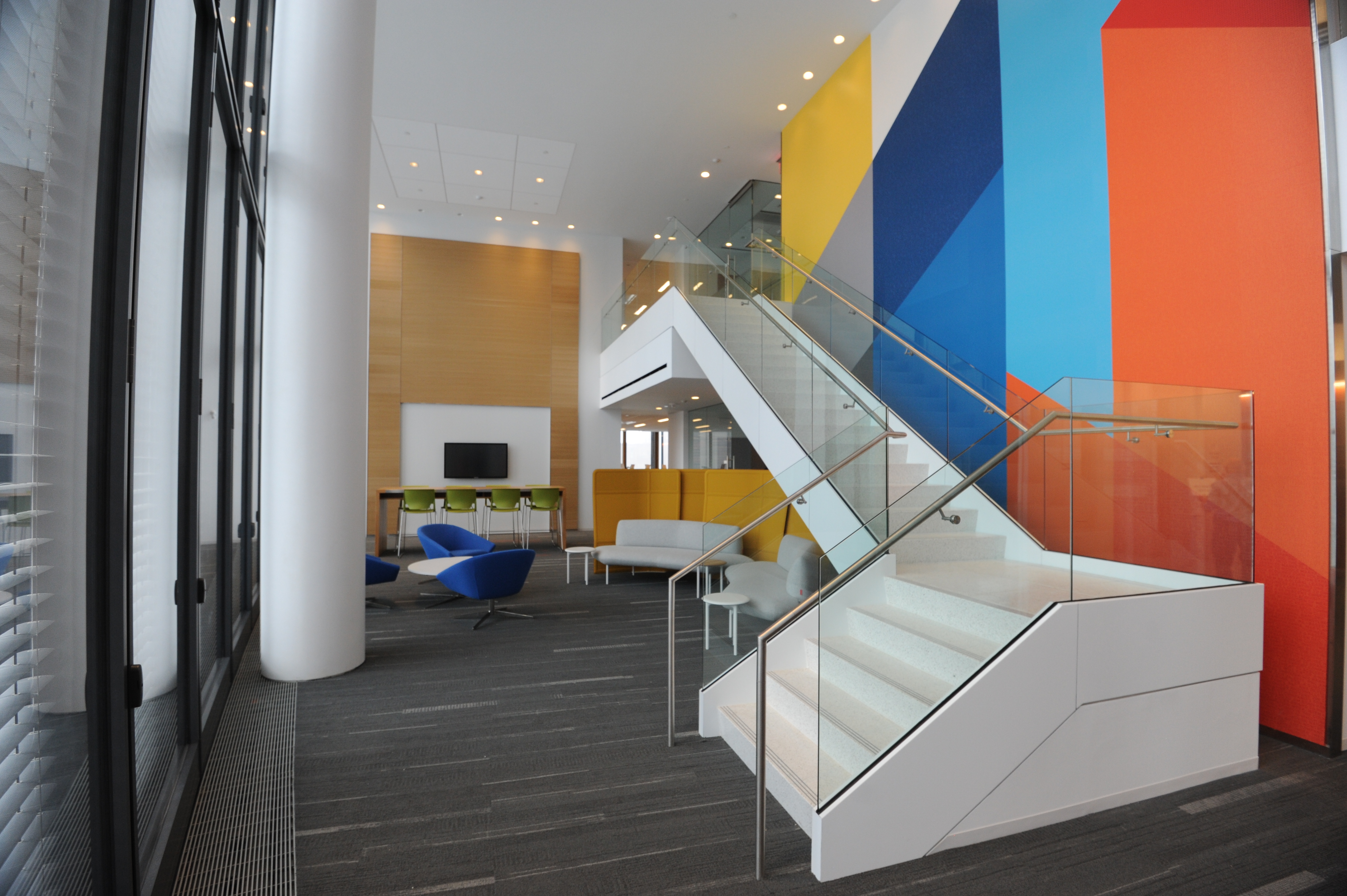 Glass stairs beside orange, blue and yellow walls in a two-story employee gathering space at the Tower at PNC Plaza