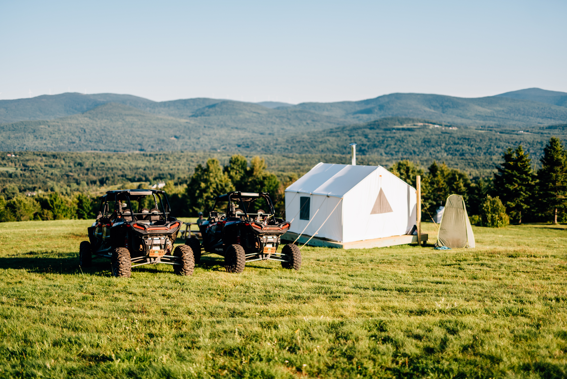 Two Polaris RZR vehicles parked beside a canvas tent overlooking mountains