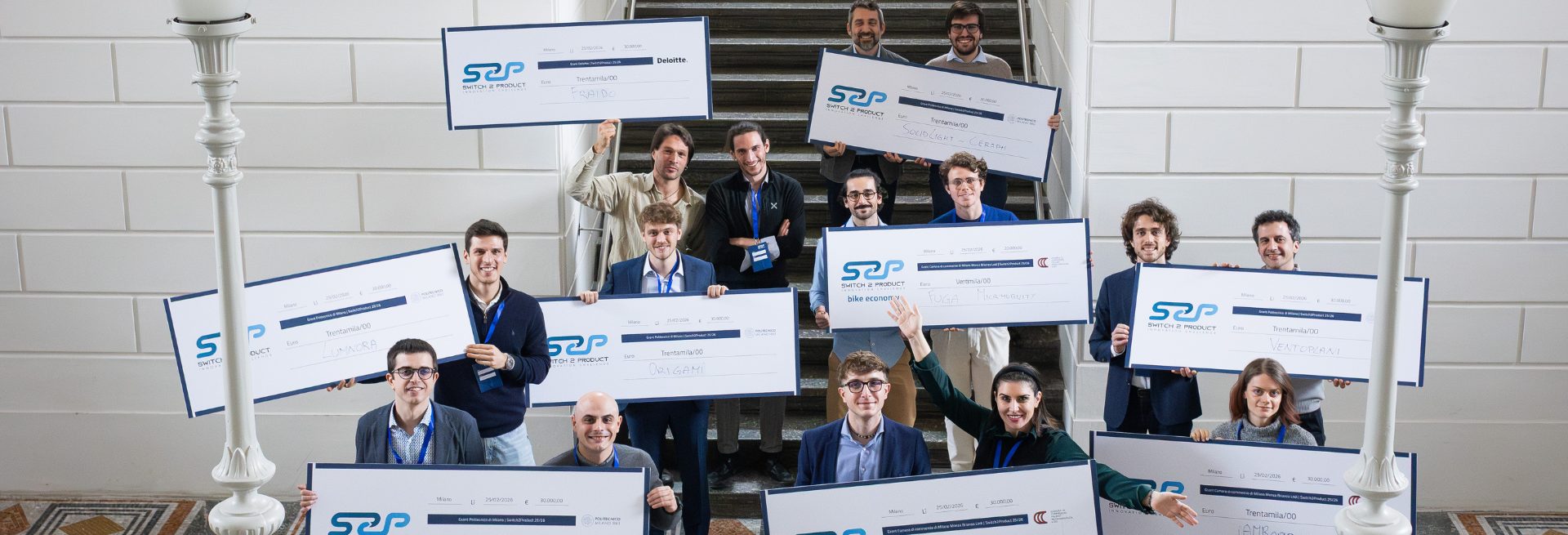 Switch2Product award recipients holding oversized grant cheques on a staircase