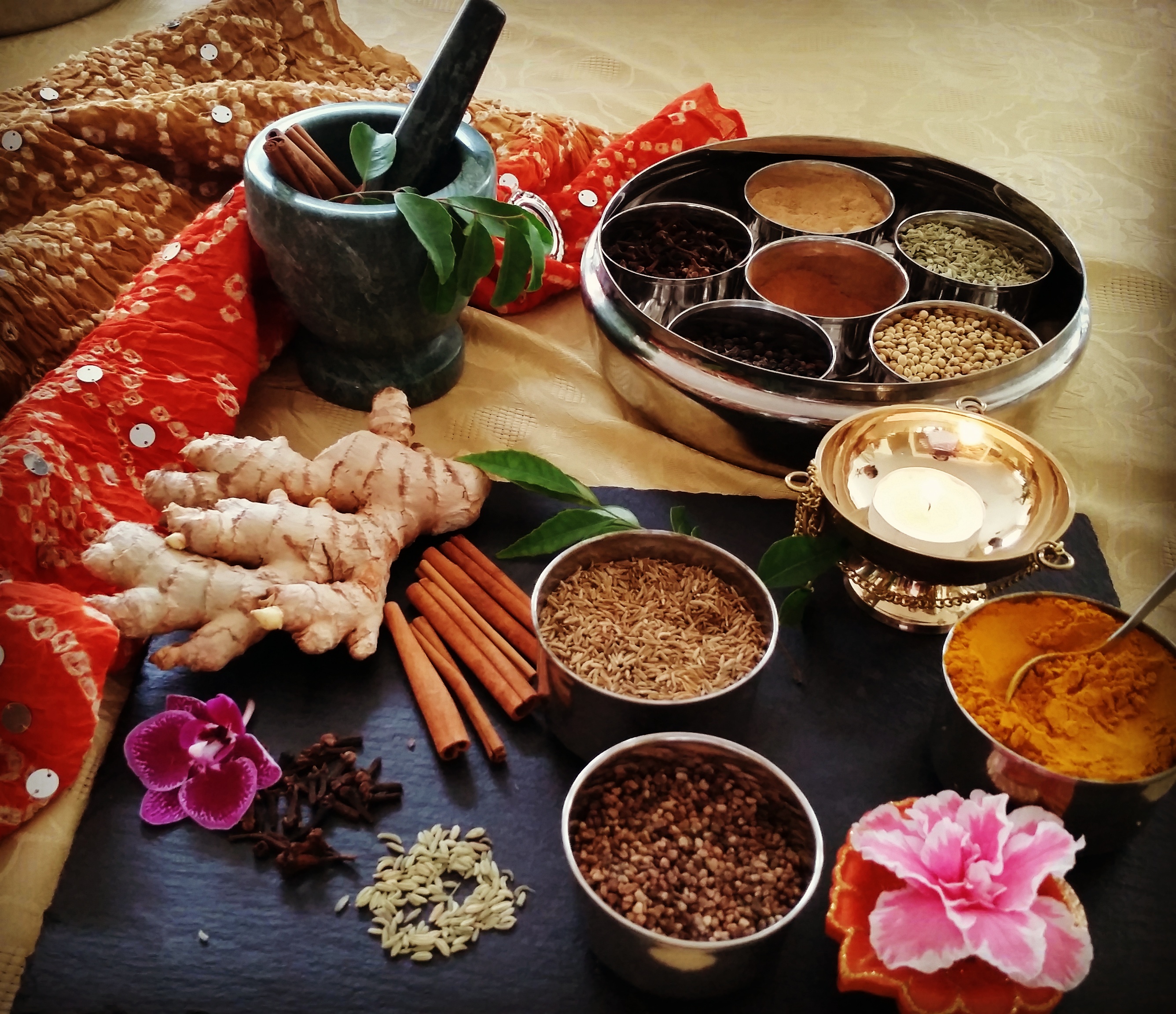 An arrangement of ginger, cinnamon, turmeric and whole spices around a mortar and pestle