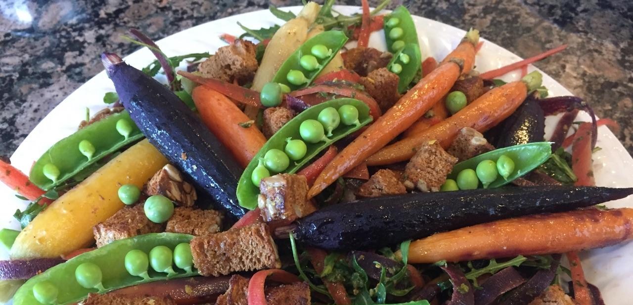 A colorful salad with whole carrots, peas, greens and toasted bread