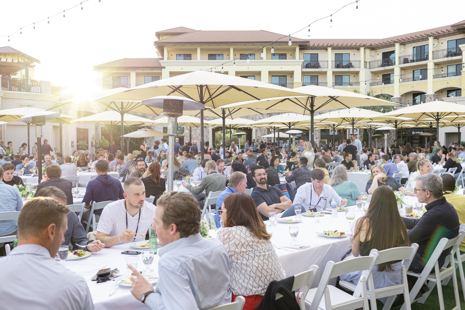 Praxis Summit participants eating and talking at outdoor tables beneath umbrellas