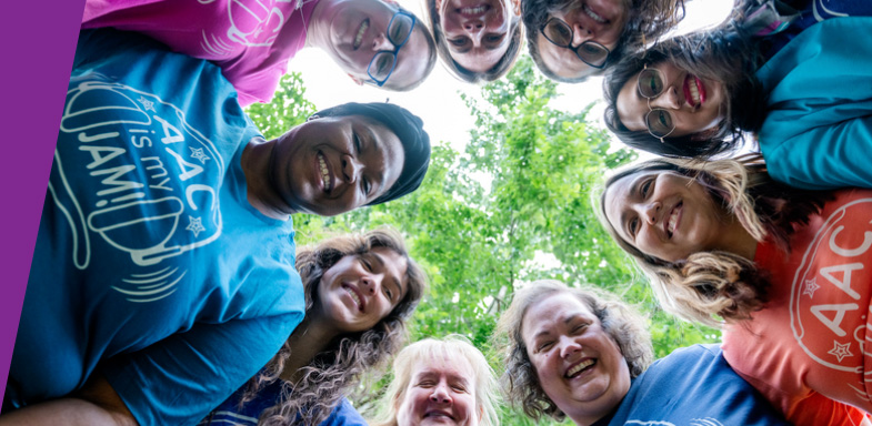 A circle of smiling people wearing colourful AAC shirts, photographed looking down toward the camera