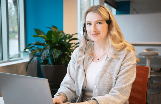 A person wearing a headset at a laptop, pictured on Precoa’s Funeral Planning Center careers page