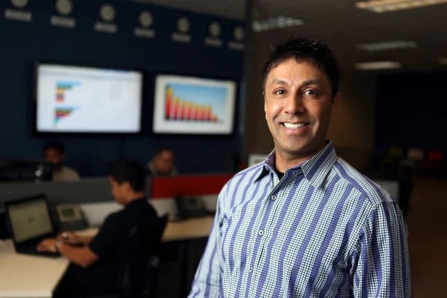 Prem Chand standing in Milestone’s Fremont managed contact center, with employees and computer displays behind him