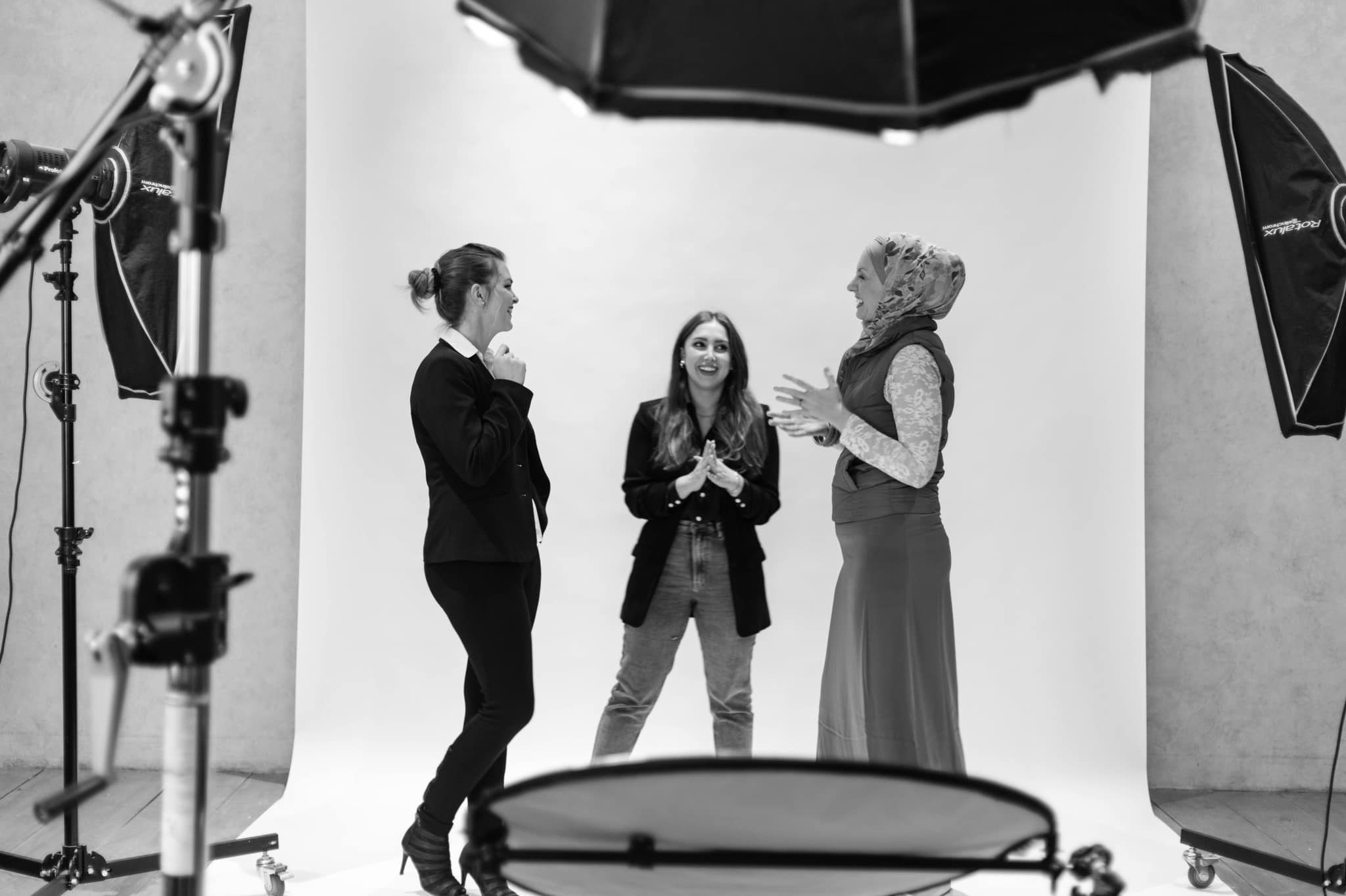 Three people talking and laughing on a photography set surrounded by studio lights