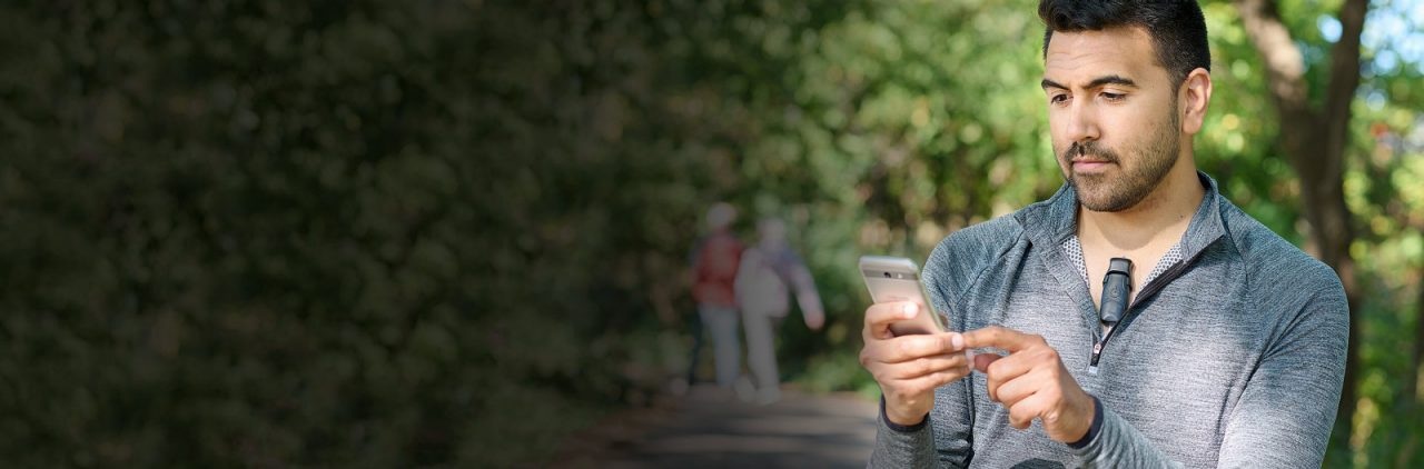 Manufacturer photograph of a man wearing a BodyGuardian monitor while using a phone outdoors