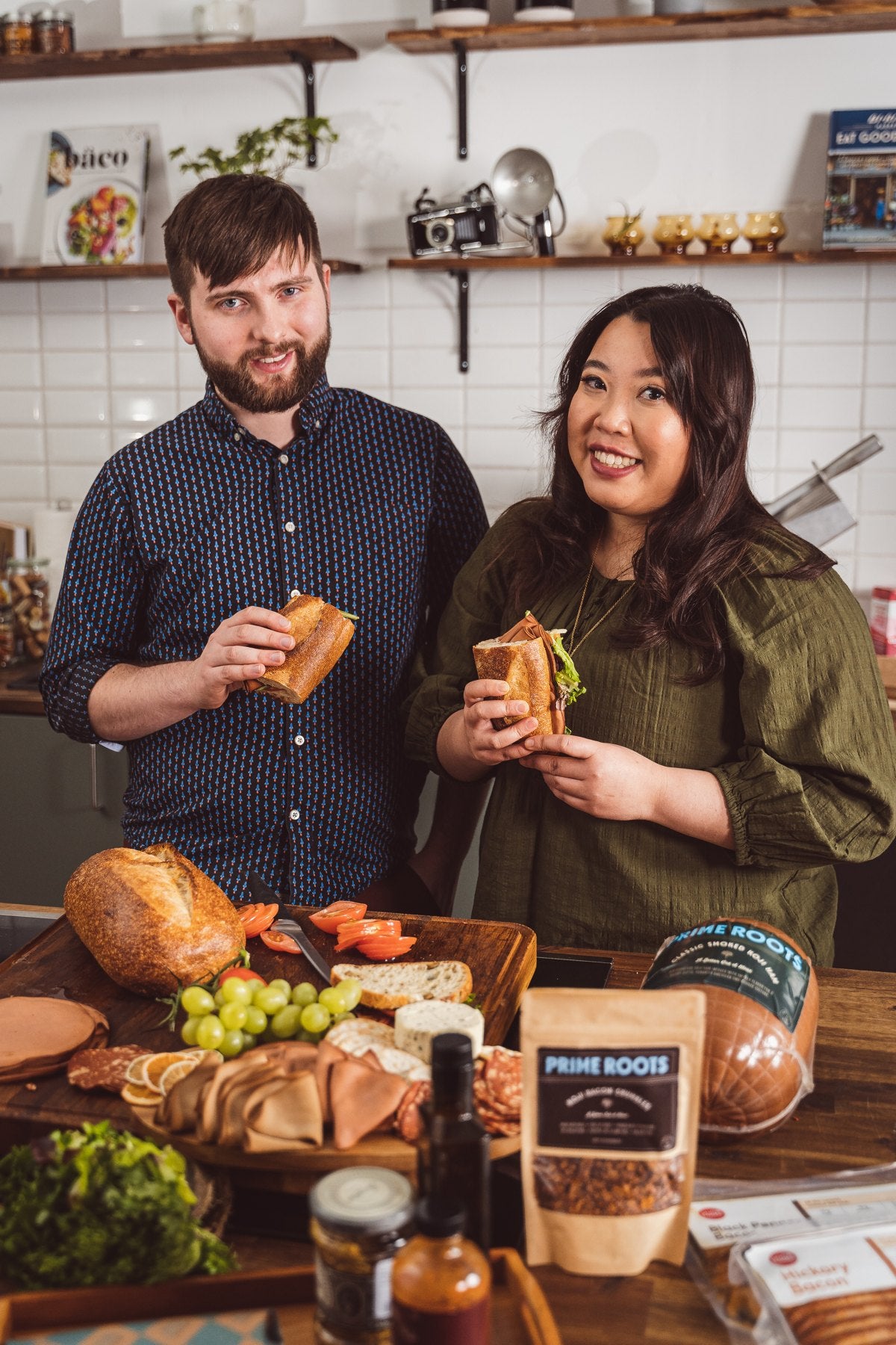 Joshua Nixon and Kimberlie Le holding sandwiches in the Prime Roots kitchen