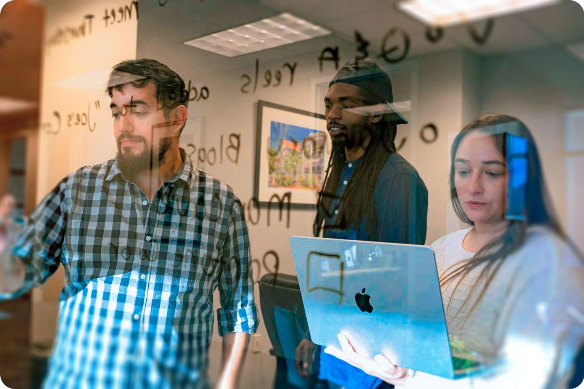Three members of the Primm Advertising team collaborating at a glass board with a laptop