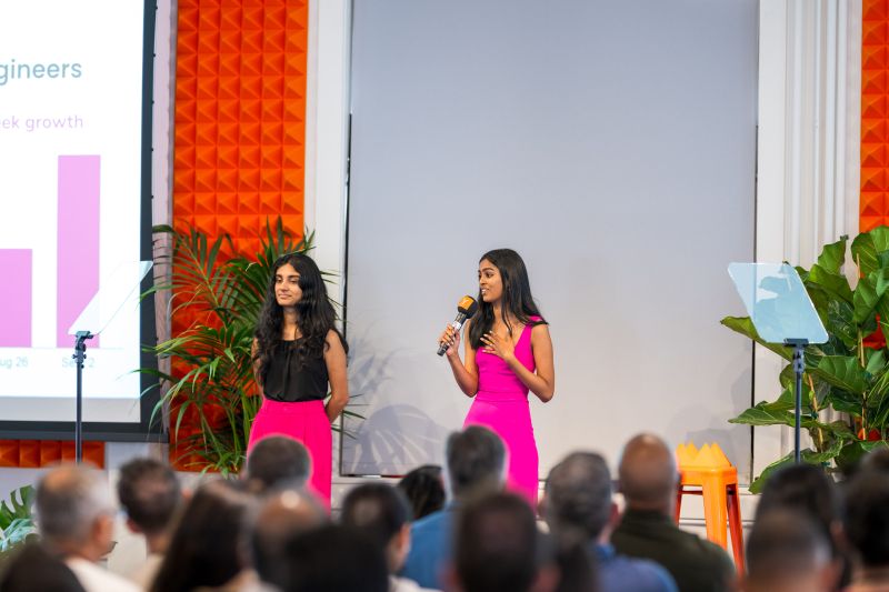 Priya Khandelwal and Priti Rangnekar onstage at Y Combinator Demo Day, dressed in hot pink