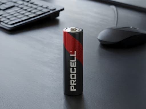 A black and red Procell alkaline battery standing beside a keyboard and mouse