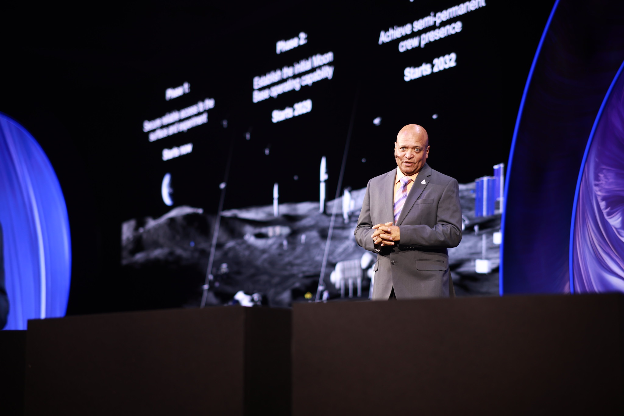 A speaker on the World Procurement Congress stage with a lunar exploration presentation behind him