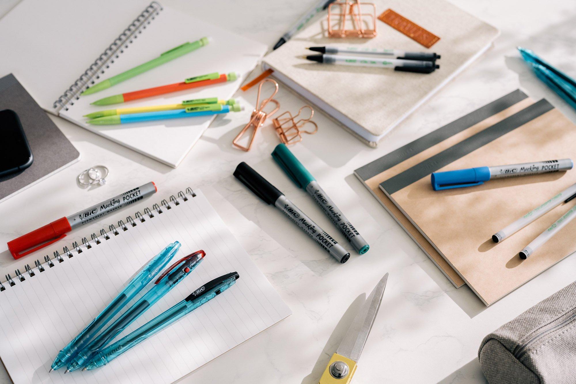 BIC pens and markers arranged across notebooks