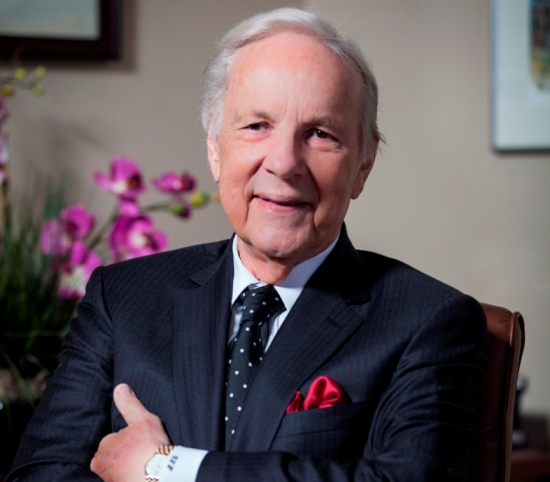 Conrad Prebys seated in a suit, with orchids behind him