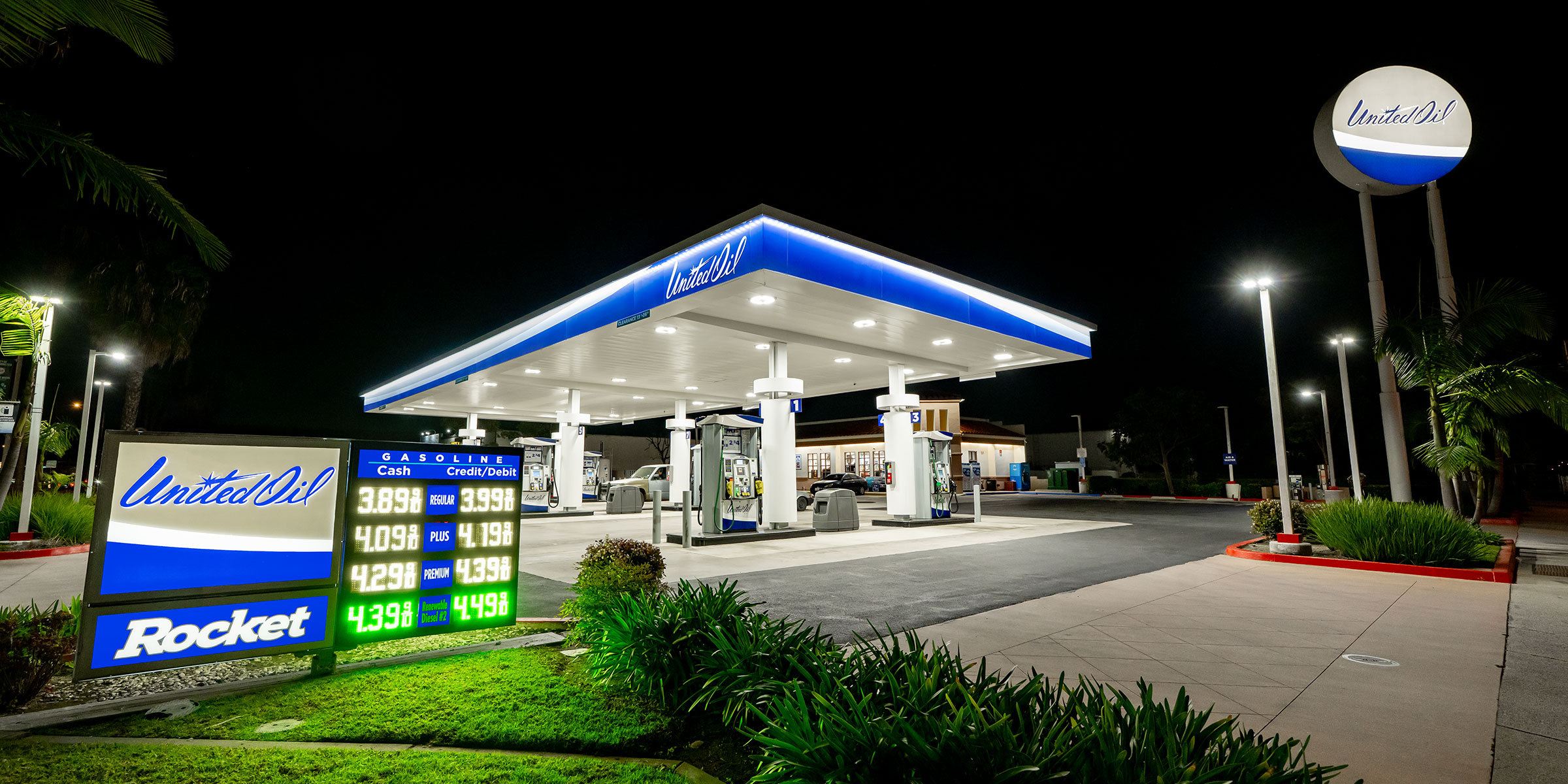 United Oil station at night with blue canopy trim, illuminated price board, and a tall circular sign