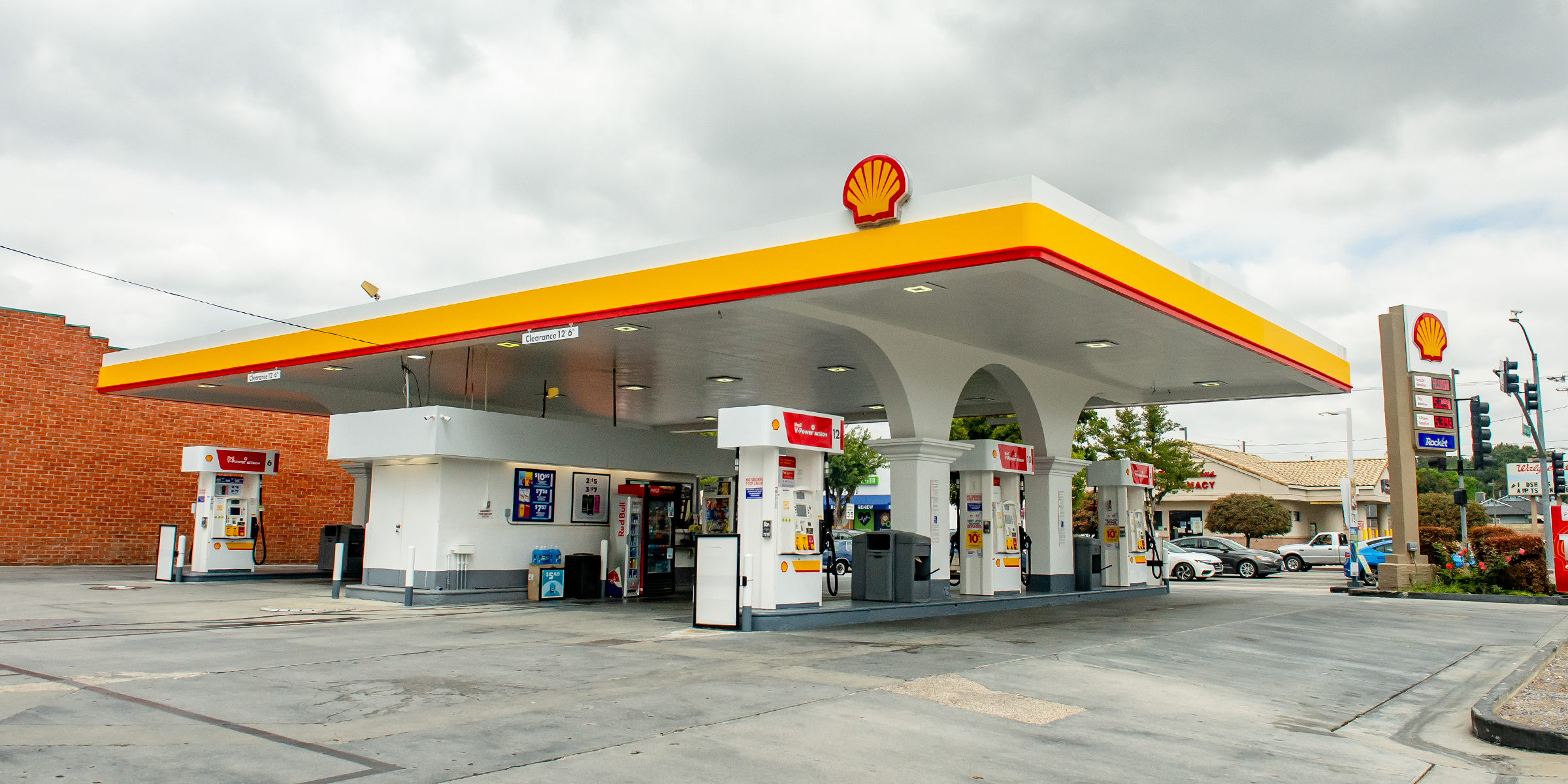 Shell station with yellow and red canopy fascia, branded fuel pumps, and roadside price sign
