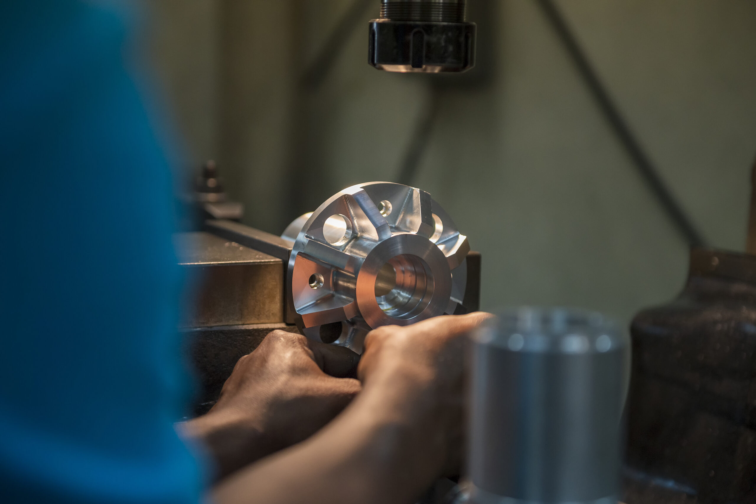 A machinist inspecting a precision-machined metal component beneath a measuring instrument