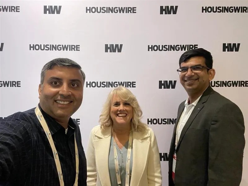 Three attendees pose together in front of a HousingWire event backdrop, in a photograph published by Prudent AI