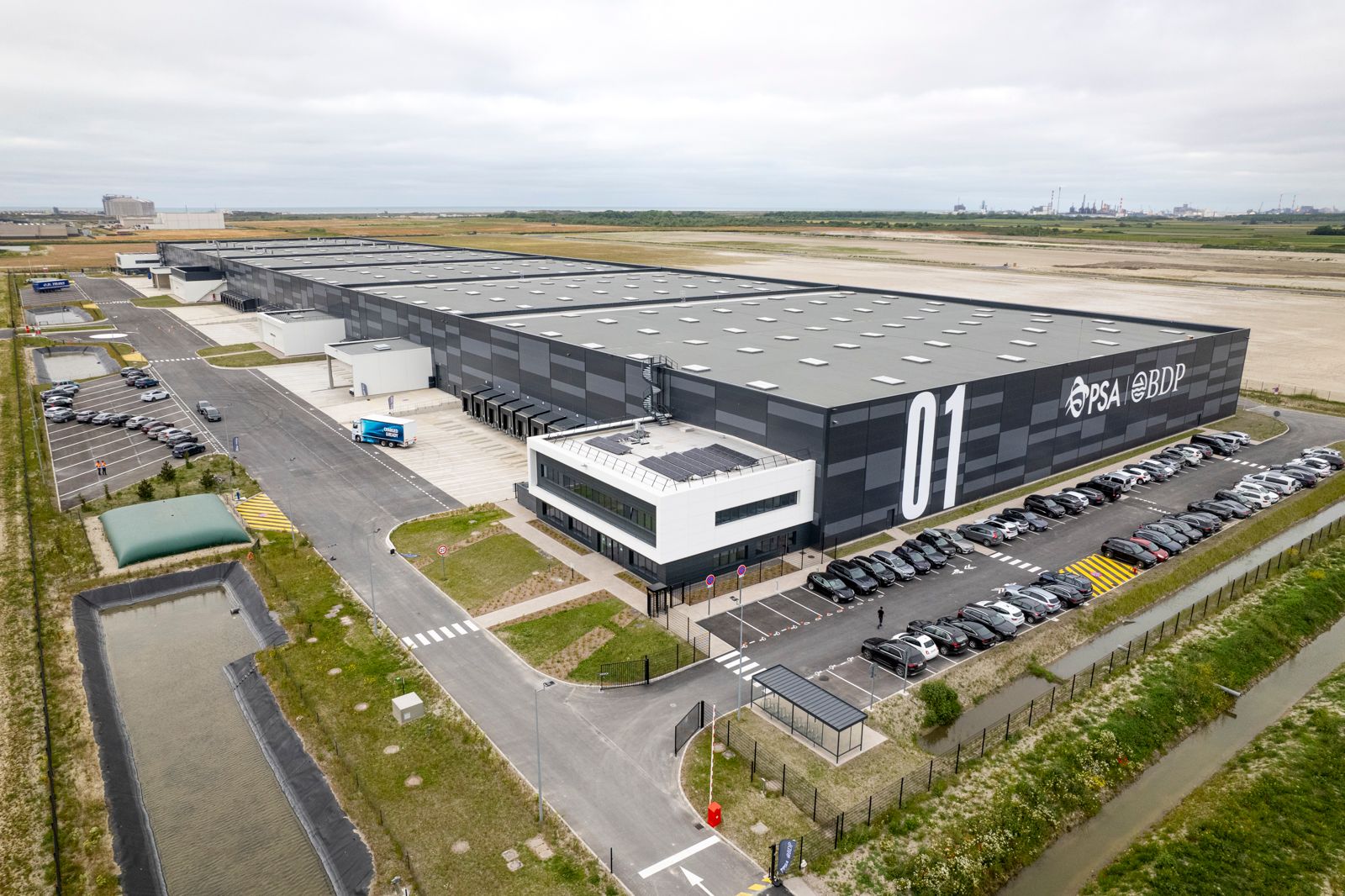 Aerial view of PSA BDP’s battery logistics warehouse in Dunkirk, with loading bays and parked vehicles