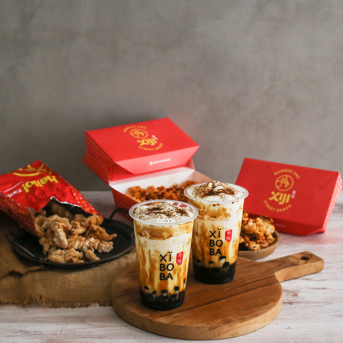 Two Xiboba drinks alongside Xi Ji fried snacks and red takeaway packaging