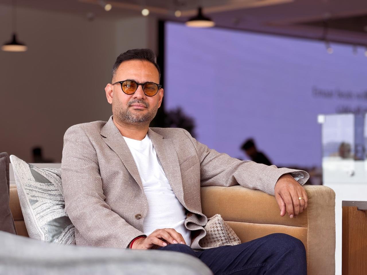 Puneet Shukla seated in a lounge, wearing a light blazer and tinted glasses