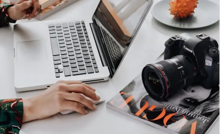 A camera, fashion magazine and laptop on a working desk