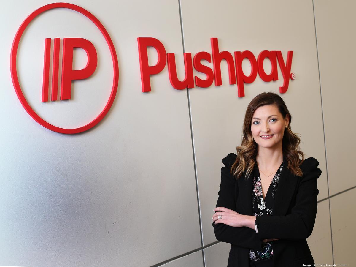 Molly Matthews standing beside Pushpay signage in its office
