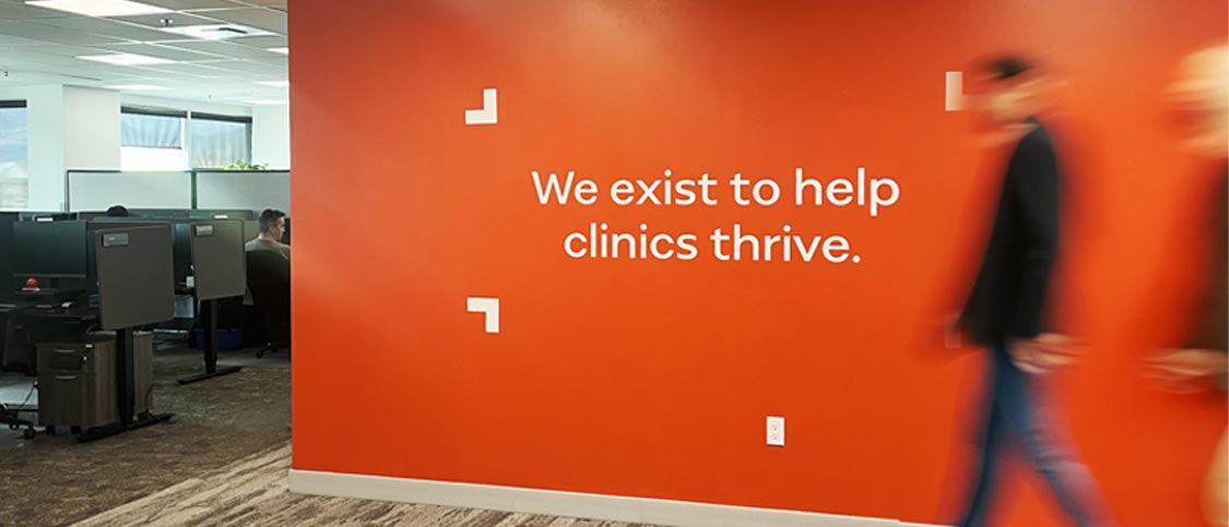 Accuro office with an orange wall reading We exist to help clinics thrive