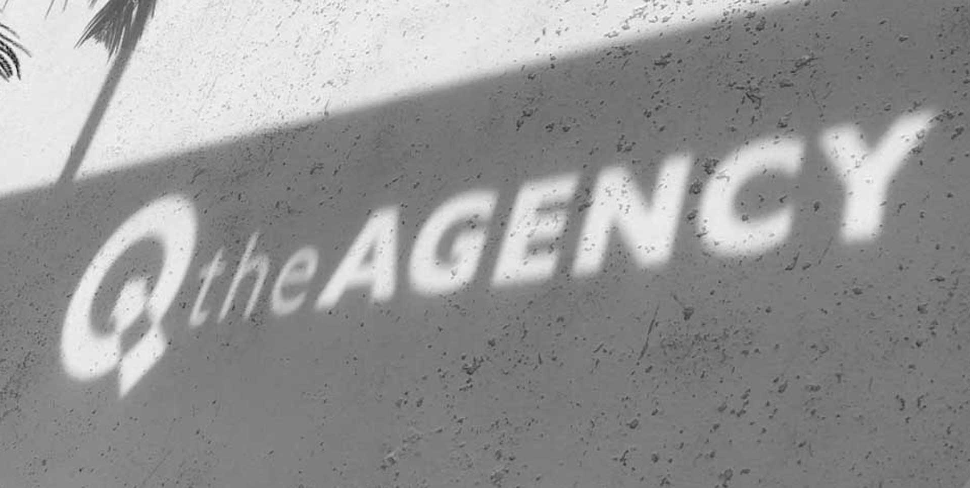 The QtheAgency name projected in light across a textured office wall