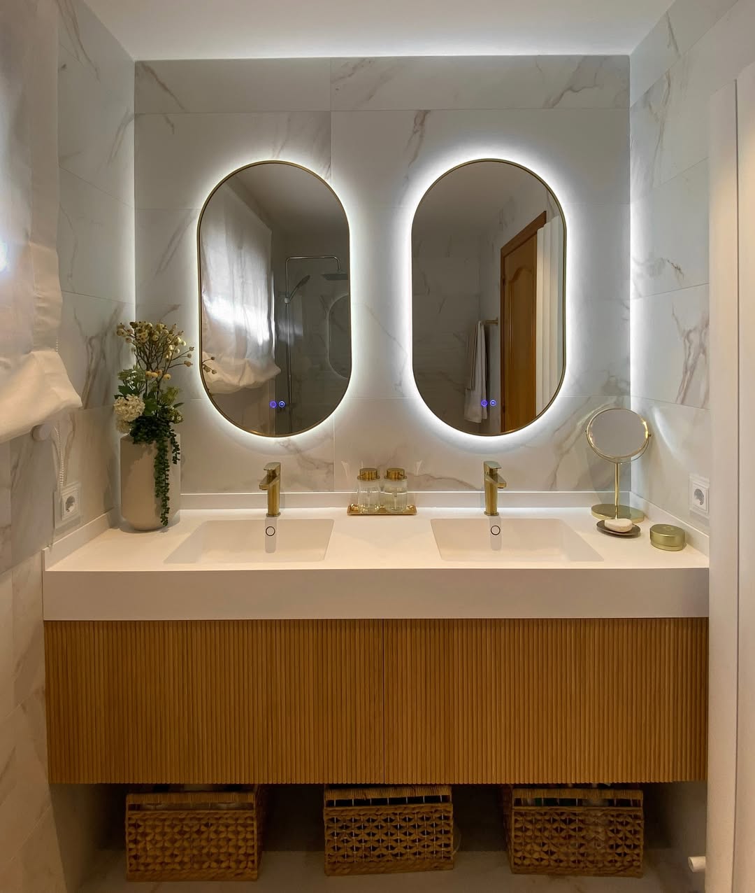 Quadratura bathroom with a wall-to-wall fluted wood vanity, two oval backlit mirrors and a white double basin