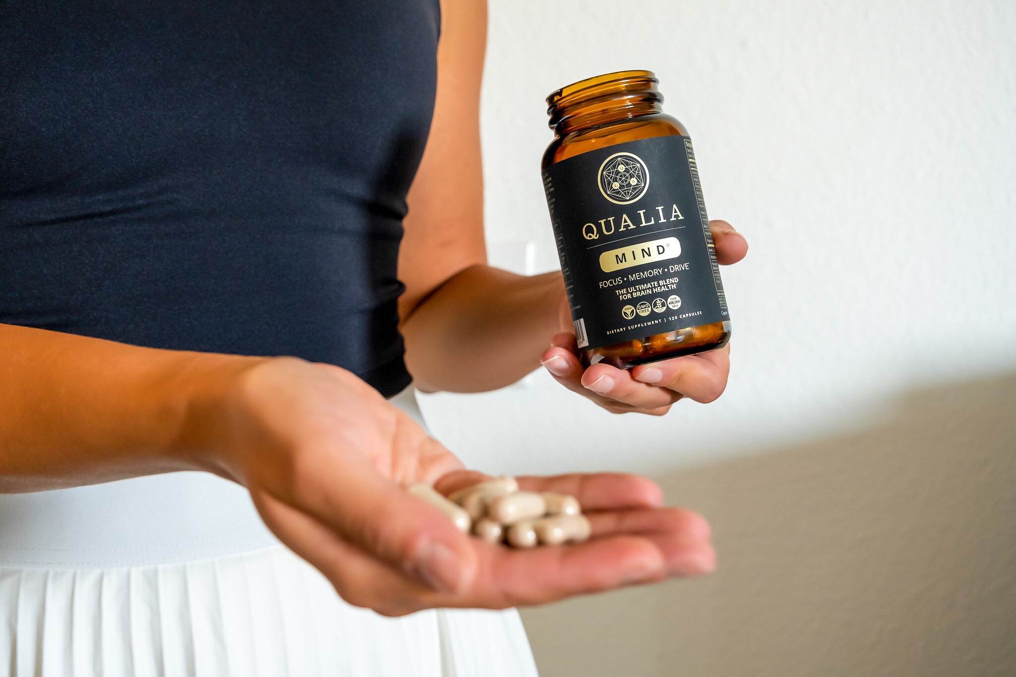 A bottle of Qualia Mind beside capsules in a hand