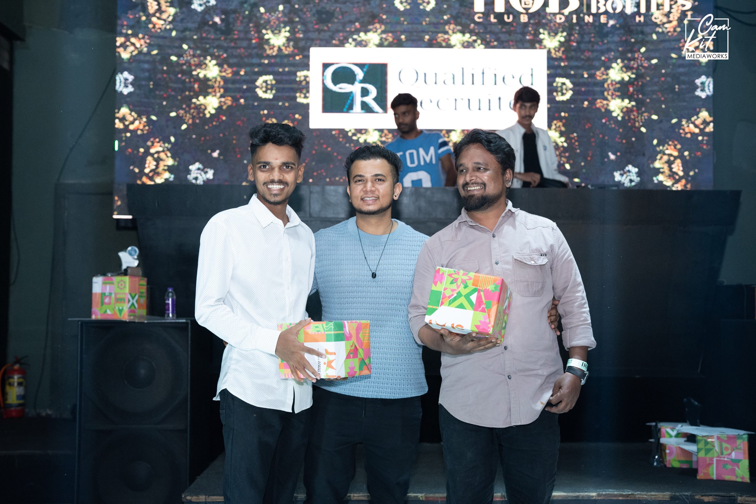 Three people pose with wrapped gifts at a Qualified Recruiter company event