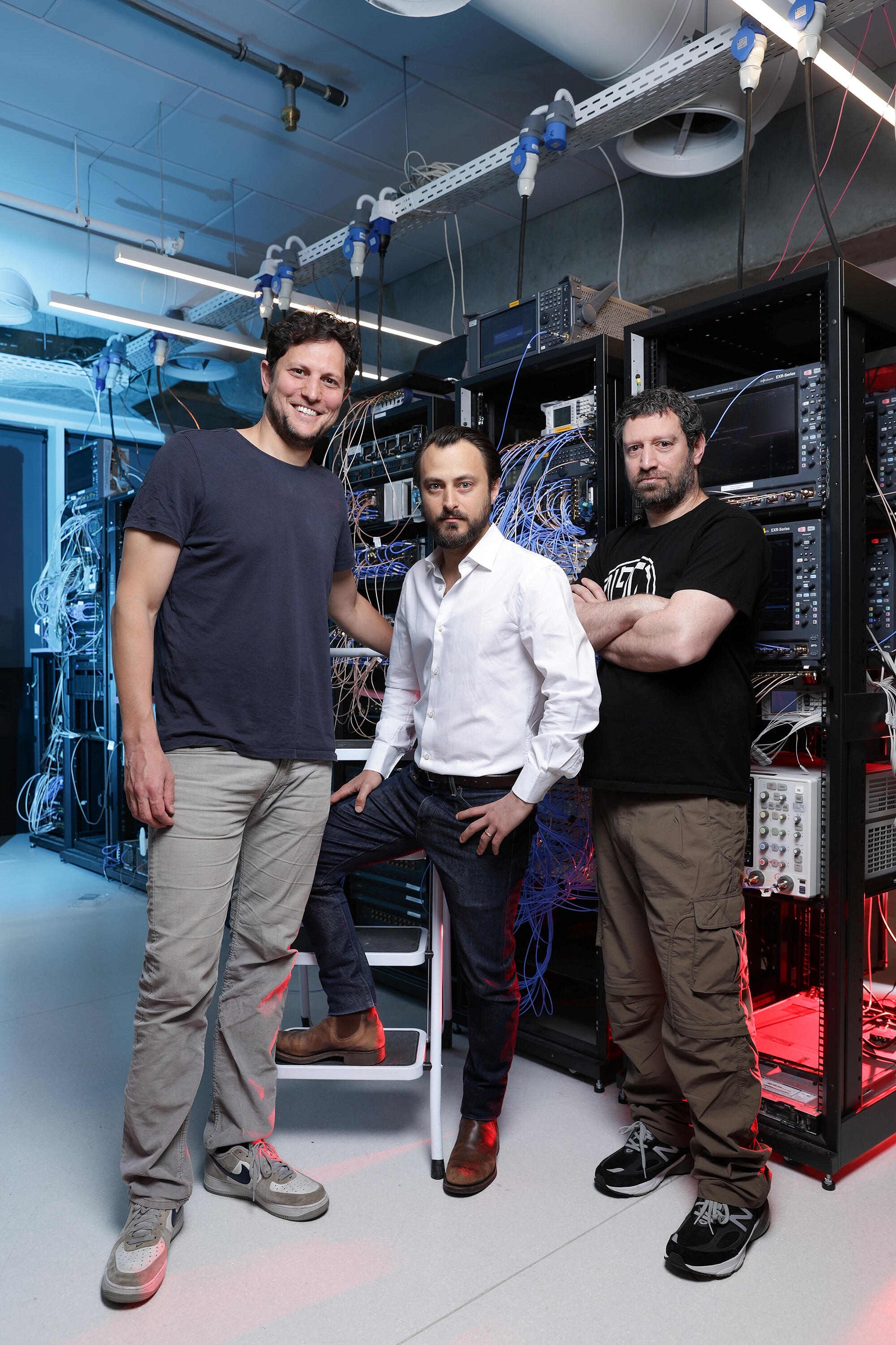 Quantum Machines’ three founders standing beside laboratory equipment racks
