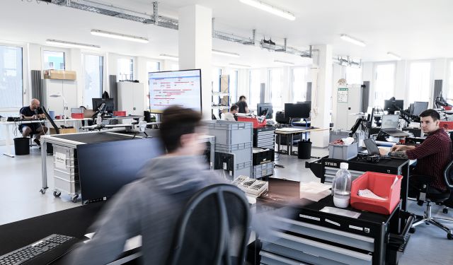Engineers and technicians work among computers and aircraft components in a Quantum Systems workspace