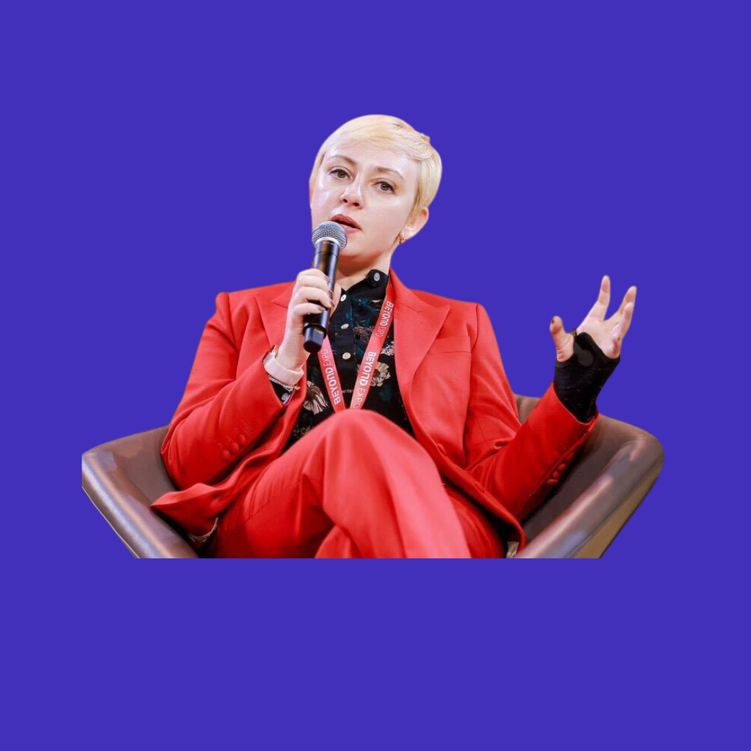 Frances Simowitz speaking into a microphone, wearing a red suit
