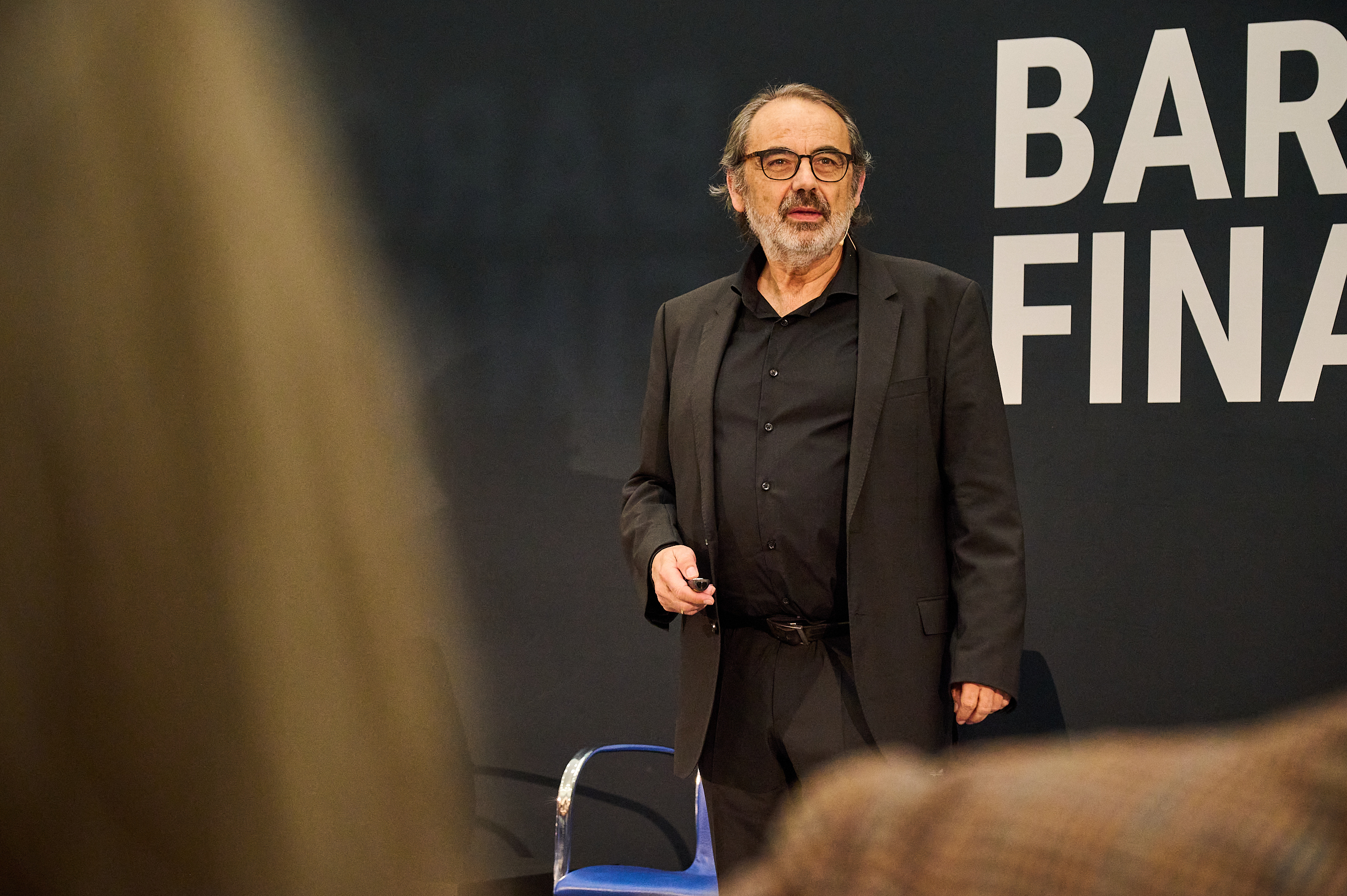 Quino Fernández speaking with a presentation remote in front of Barcelona Finance Hub signage