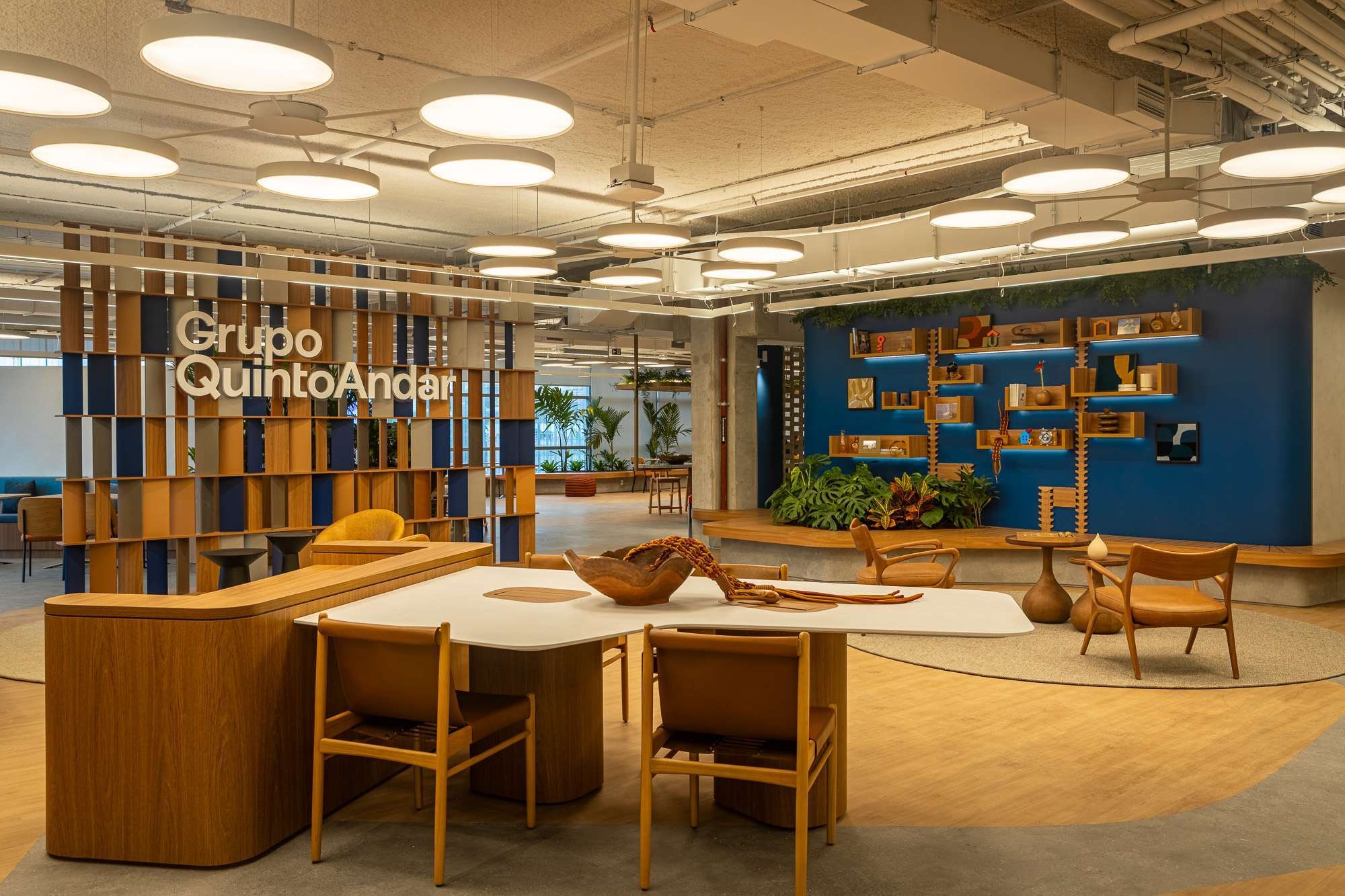 Wooden tables, shelving and circular ceiling lights in the Vila QuintoAndar office