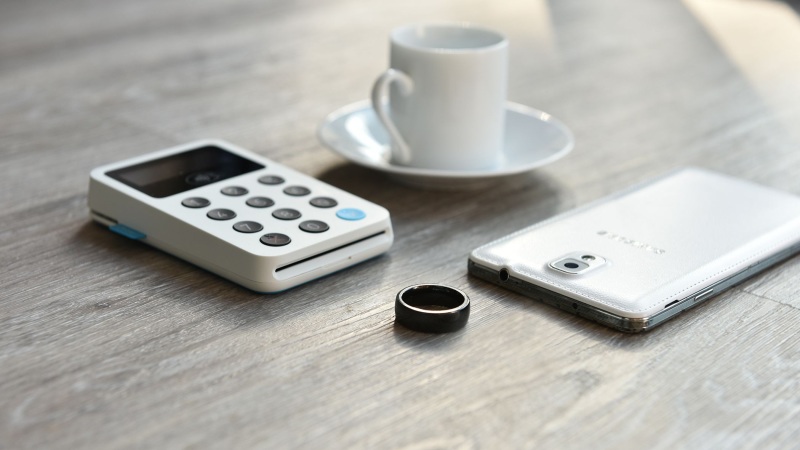 Quontic’s black payment ring beside a smartphone, payment terminal and coffee cup