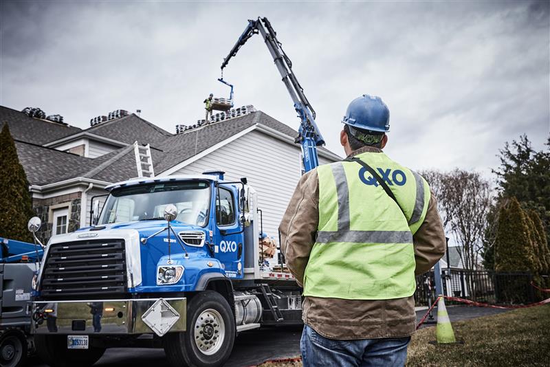 QXO employee supervising a boom-truck delivery of materials onto a residential roof