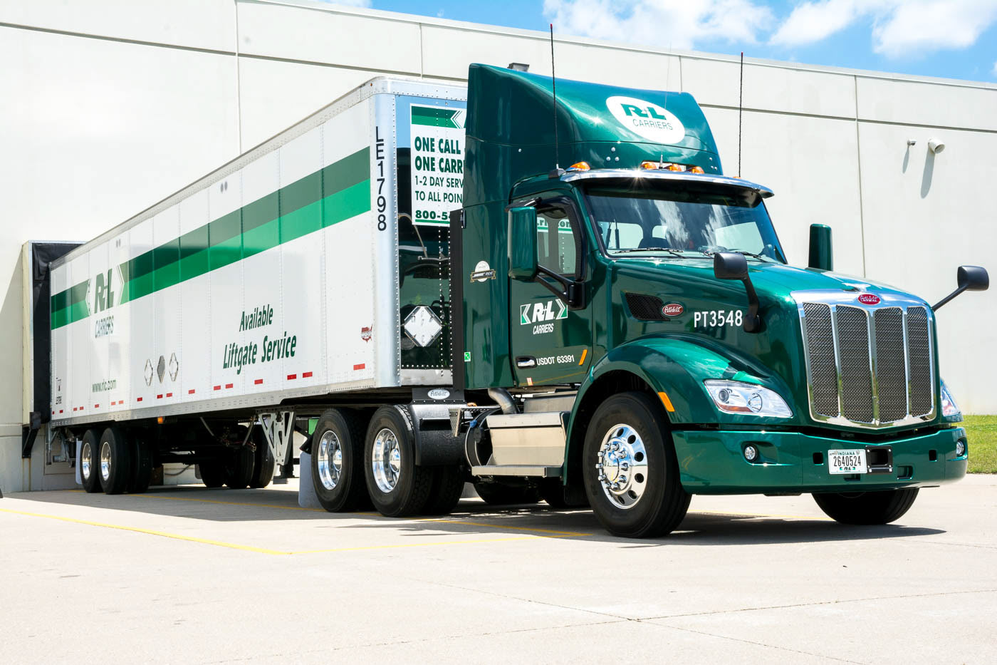 Green R+L tractor and white freight trailer parked at a loading dock