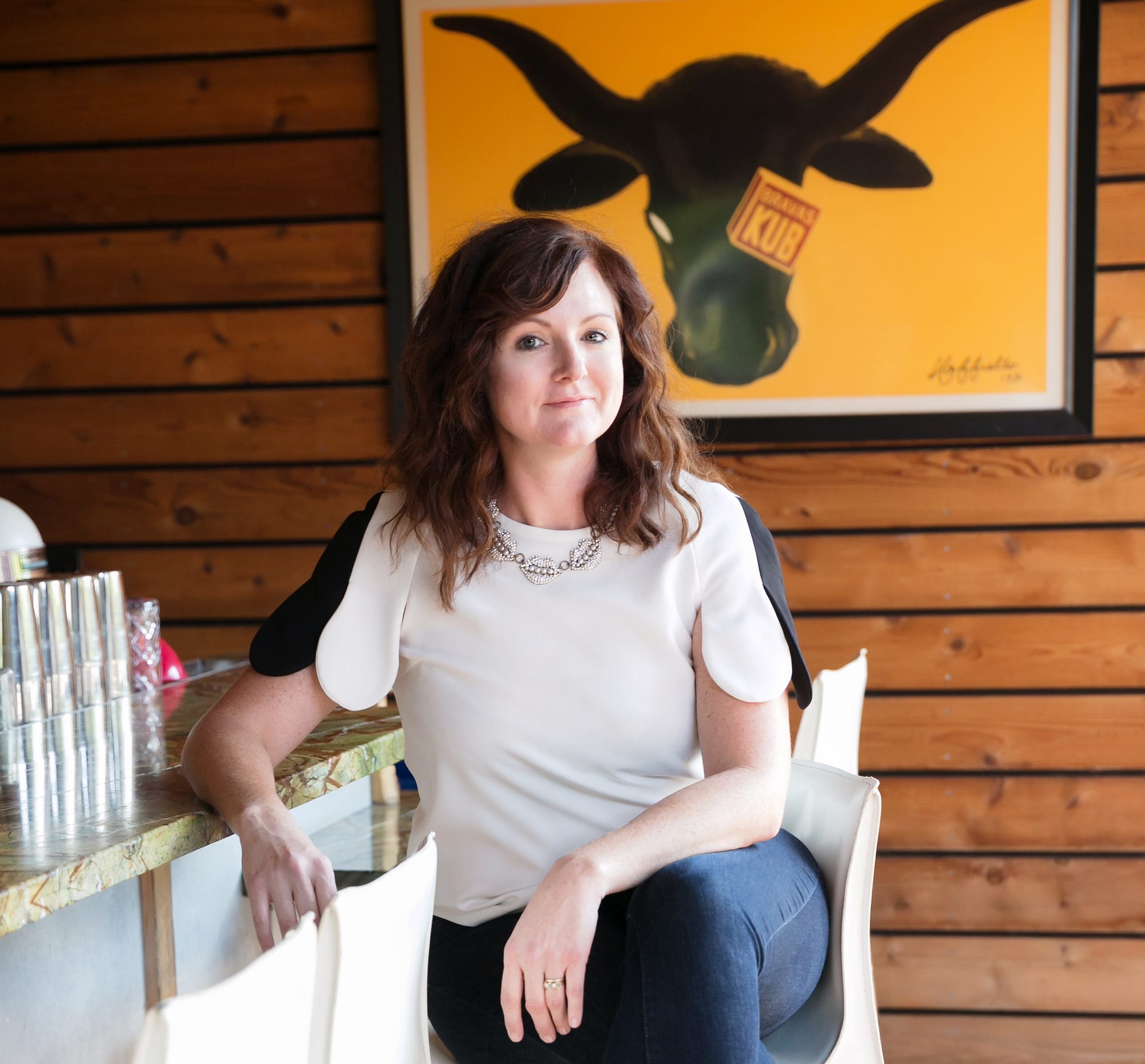 Rachel Ayotte seated at a restaurant bar beneath a bright bull artwork