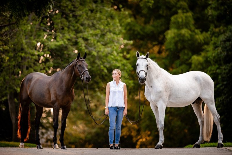 Rachel Truair standing outdoors between a dark brown horse and a gray horse