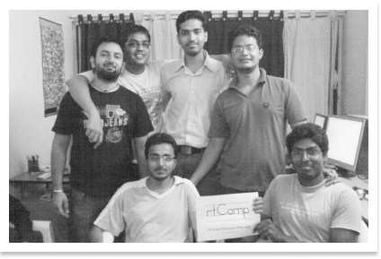 Black-and-white photograph of rtCamp’s founding team gathered around a small rtCamp sign