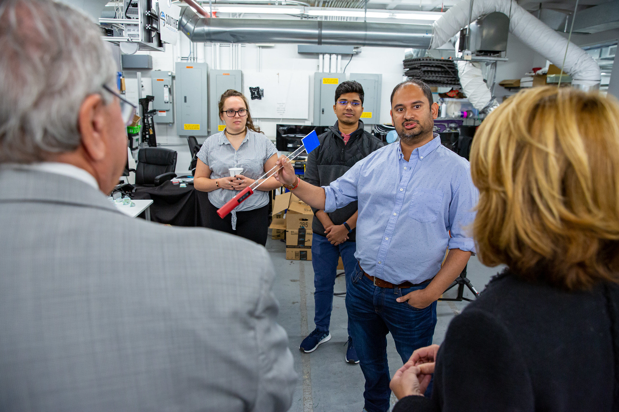 Rahul Chipalkatty demonstrating Southie Autonomy's handheld robot-teaching interface to visitors in a robotics lab