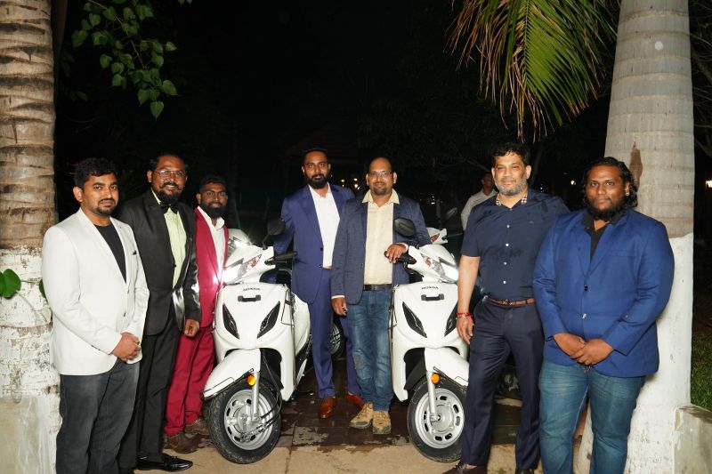 A group gathered around two white Honda scooters in a SwankTek recognition-event photograph