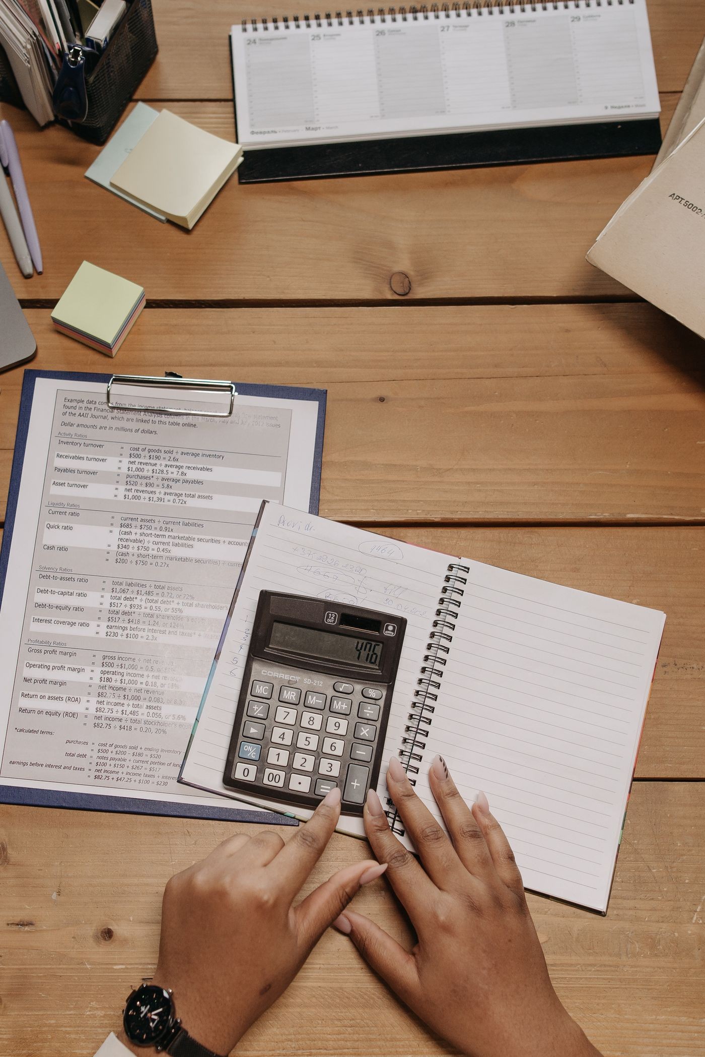 Hands using a calculator beside a notebook and financial paperwork