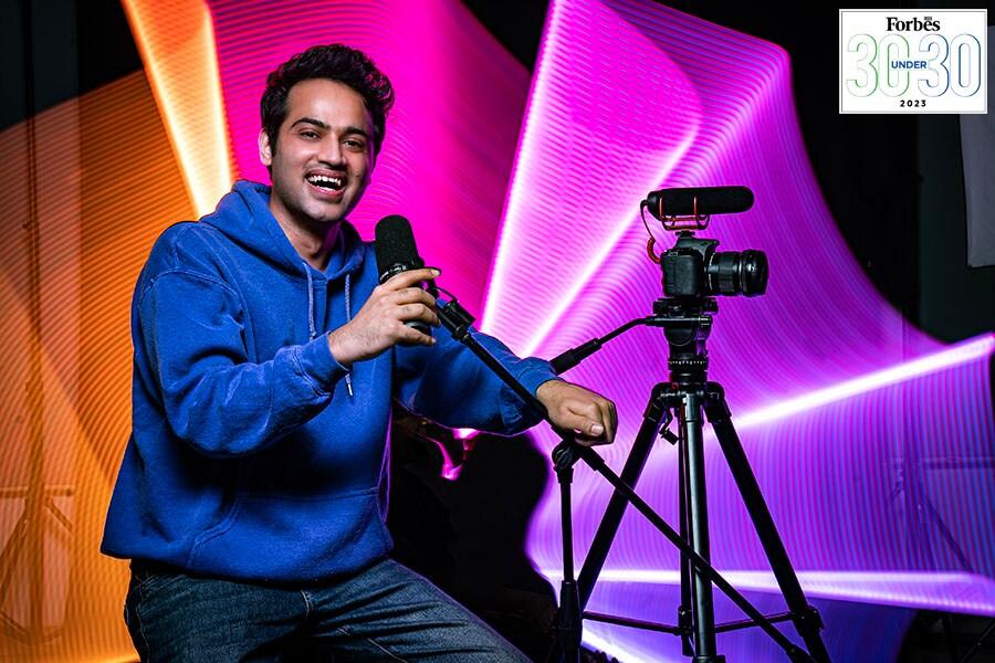 Raj Shamani with a microphone and camera in a colorful studio setting
